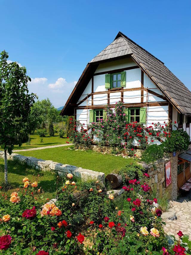 Cottage and lawn with red, orange, and purple flowers decorating the perimeter