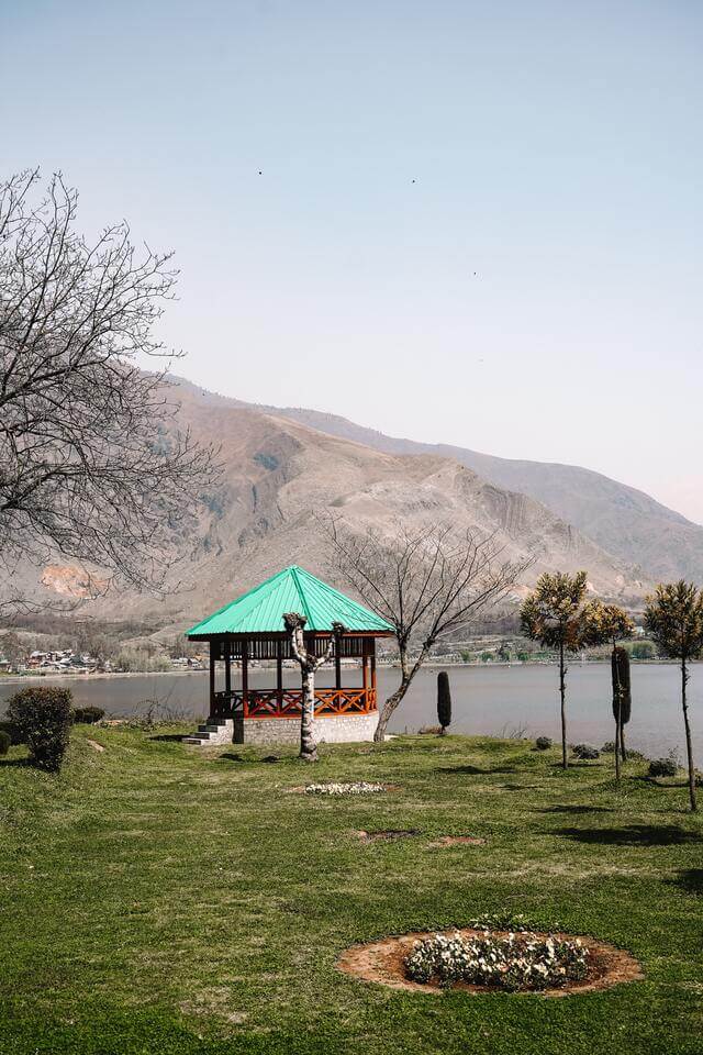 Garden during winter/early spring with flower patches and a gazebo at the back with a lake and mountain on the other side