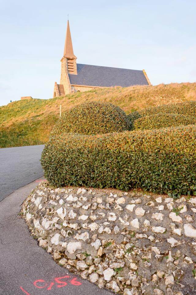 Neatly cut hedges along a curved road with a church int the background