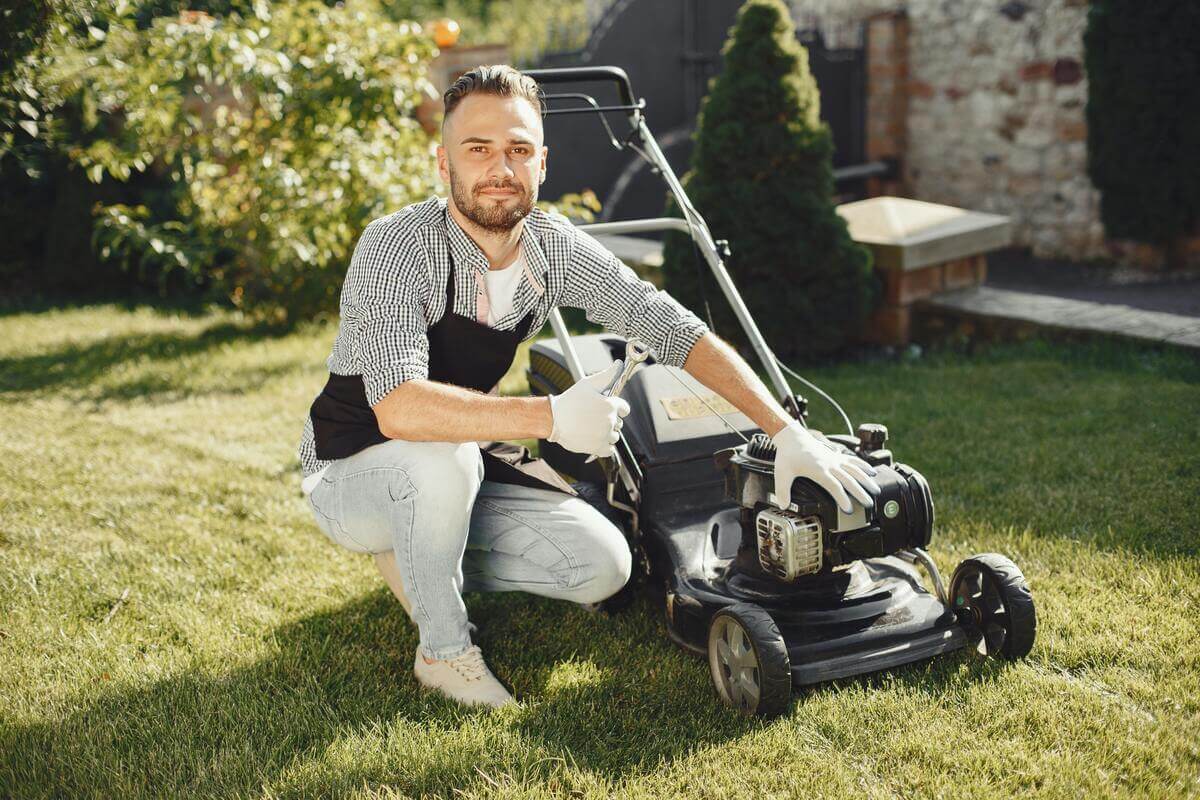 Man crouched down beside his lawnmower posing for the camera on a freshly cut lawn